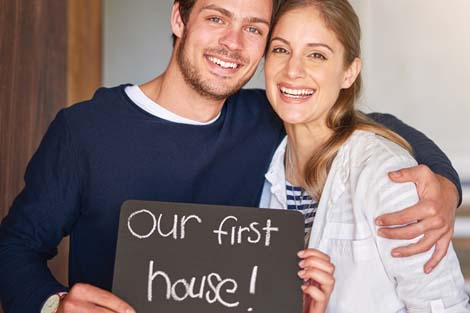 A couple holding a sign that reads "Our first home"