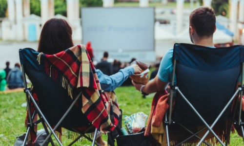 A couple sitting in camp chairs on a lawn watching a movie