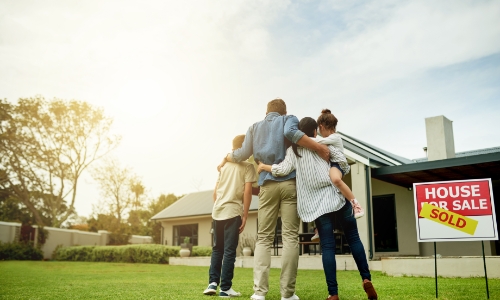 A family hugging in front of a house with a sold sign