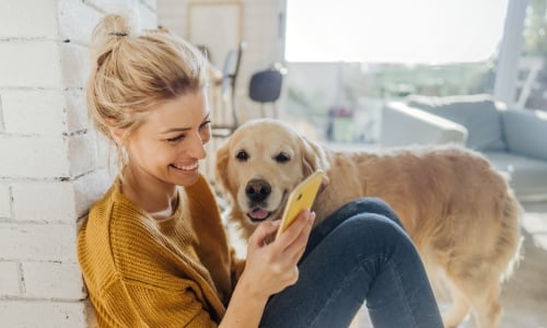 A woman smiling at her cell phone and petting her dog