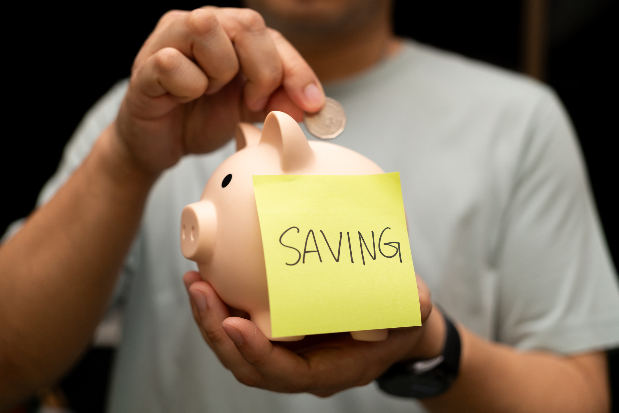 Man putting a coin in a piggy bank with a sticky note labeled “saving”