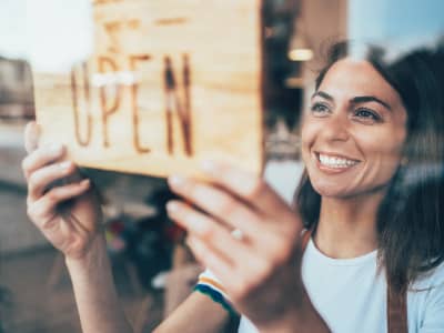 Portrait of a happy business owner hanging an open sign on the door at a cafe and smiling.