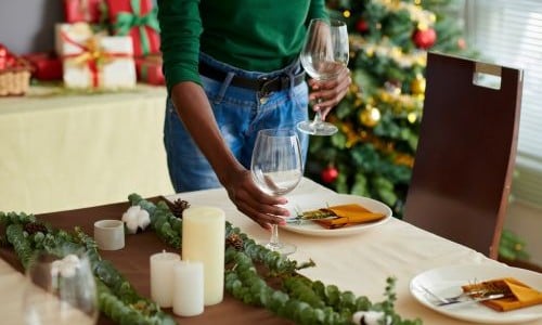 A person setting the table for a Christmas gathering surrounded by presents, greenery, and candles