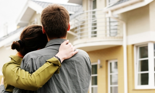 A young couple hugging in front of a house