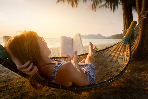 woman sitting in a hammock by the ocean and reading a book