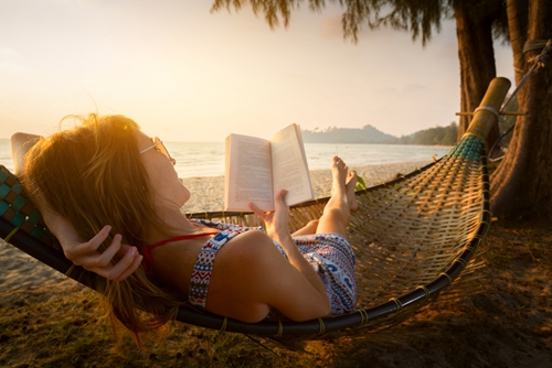 woman sitting in a hammock by the ocean and reading a book woman sitting in a hammock by the ocean and reading a book